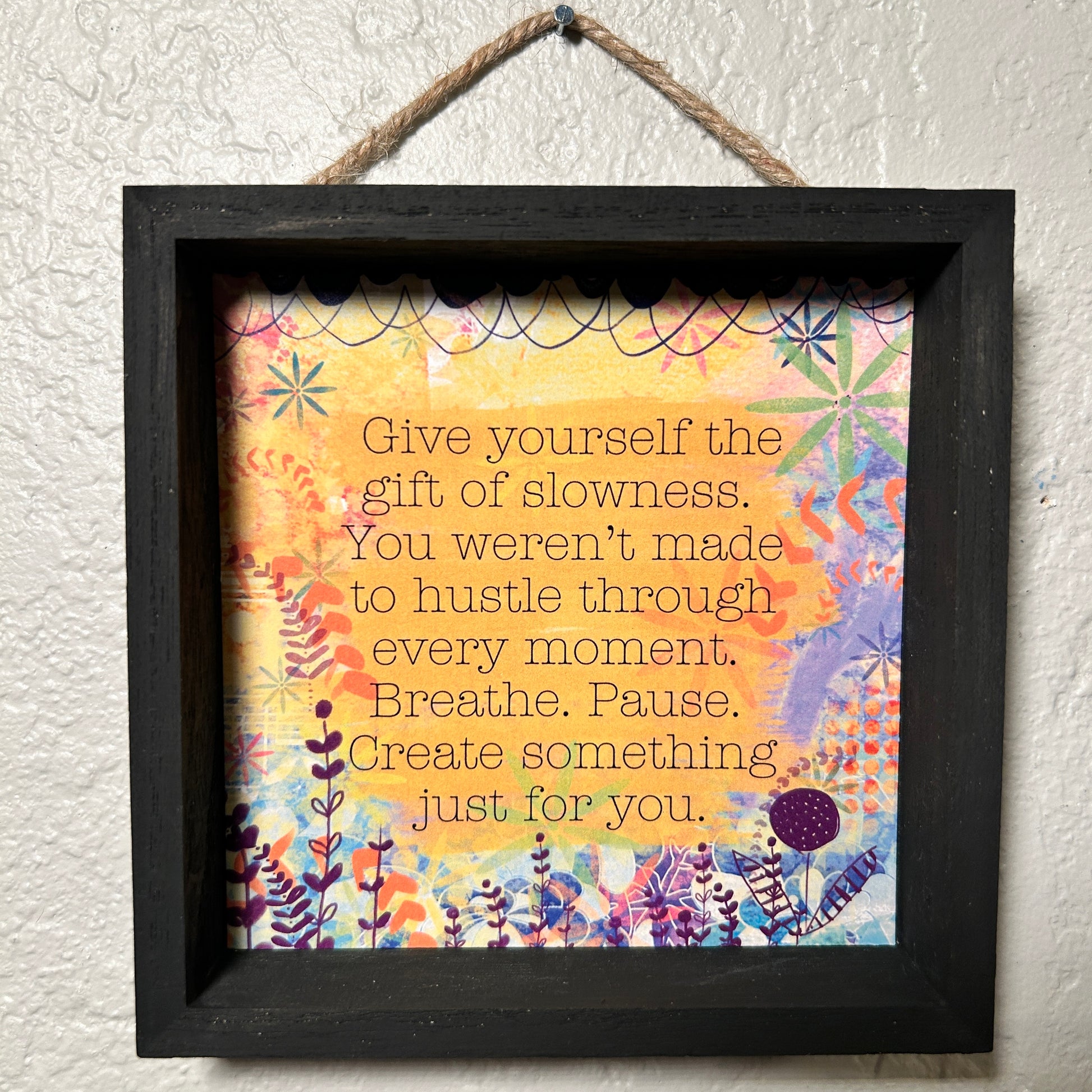 Framed motivational quote with colorful floral design on a textured wall.