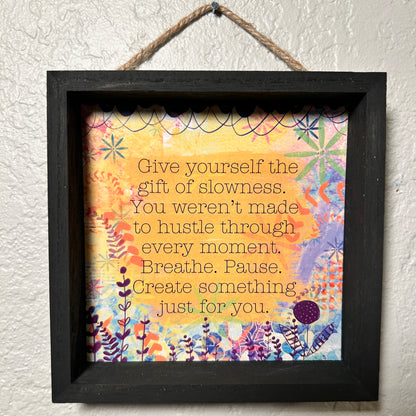 Framed motivational quote with colorful floral design on a textured wall.