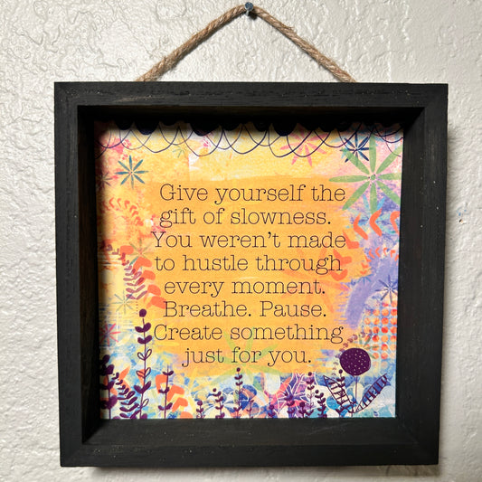 Framed motivational quote with colorful floral design on a textured wall.